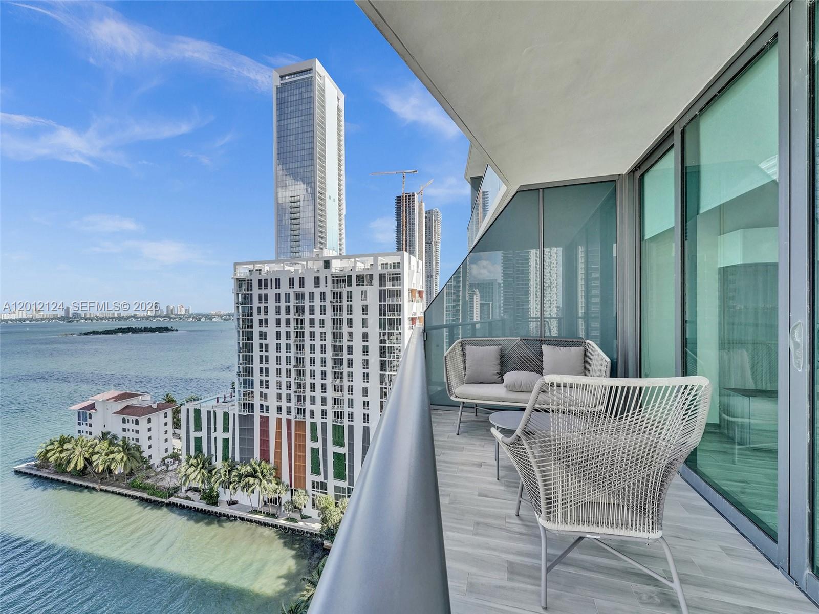 A balcony with outdoor furniture overlooks a bay, a white building, and city skyscrapers — 460 NE 28th St # 1701, Miami FL 33137, MIAMI, FL
