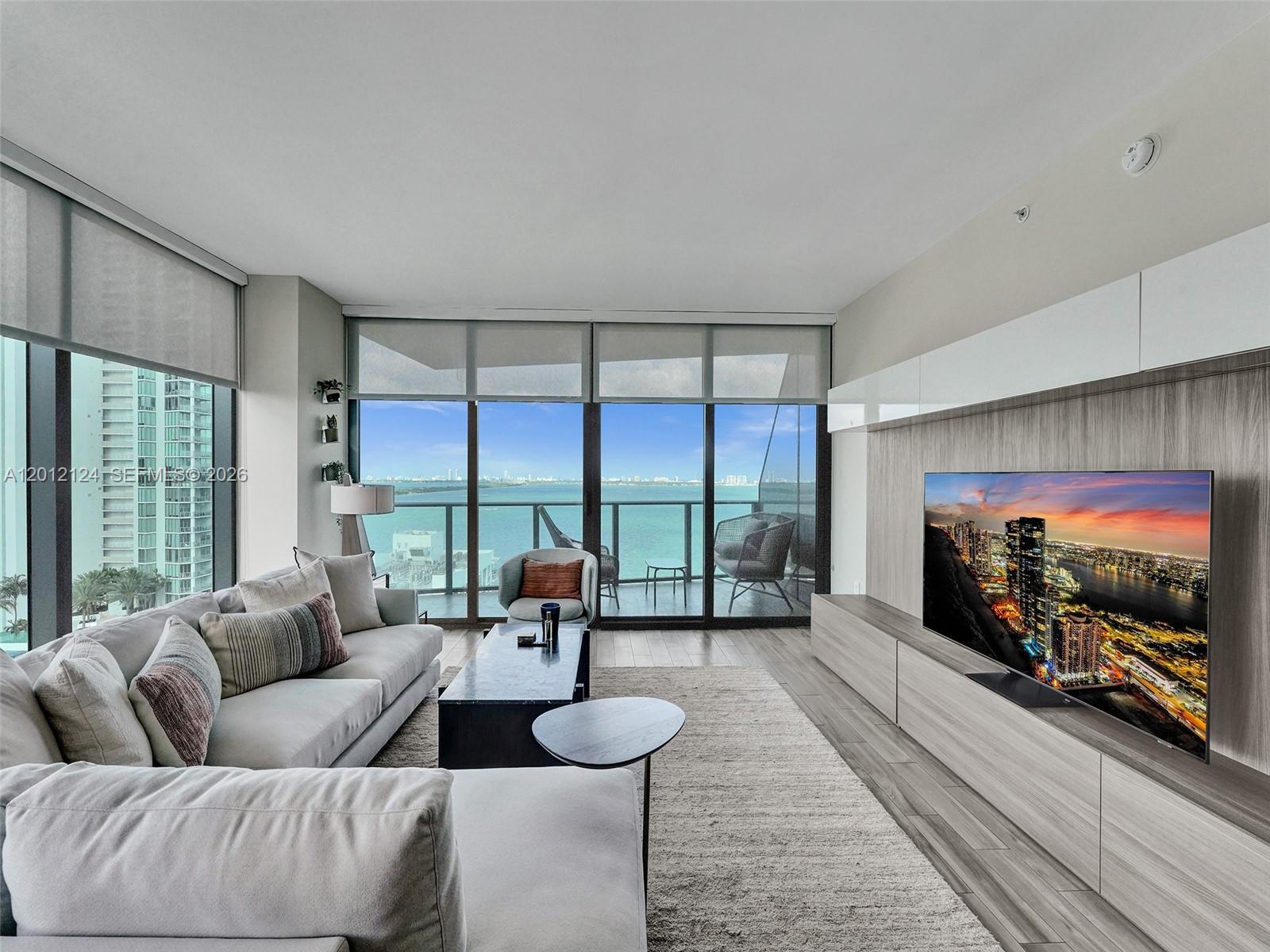A modern living room features a large sectional sofa, media console, and floor-to-ceiling balcony windows — 460 NE 28th St # 1701, Miami FL 33137, MIAMI, FL