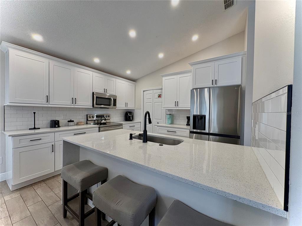 A modern kitchen features white cabinets, quartz countertops, a central island, and stainless steel appliances — 154 CASTLEMAIN CIRCLE, DAVENPORT, FL