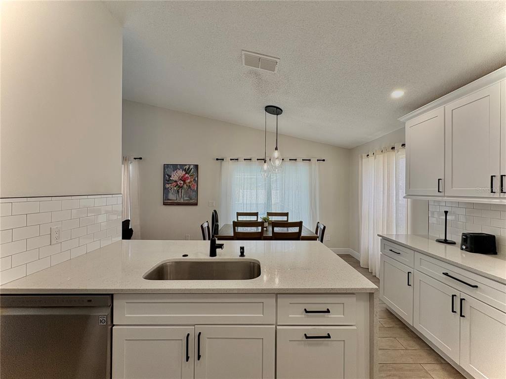 A kitchen with white cabinets, quartz countertops, and a subway tile backsplash overlooks a dining area — 154 CASTLEMAIN CIRCLE, DAVENPORT, FL