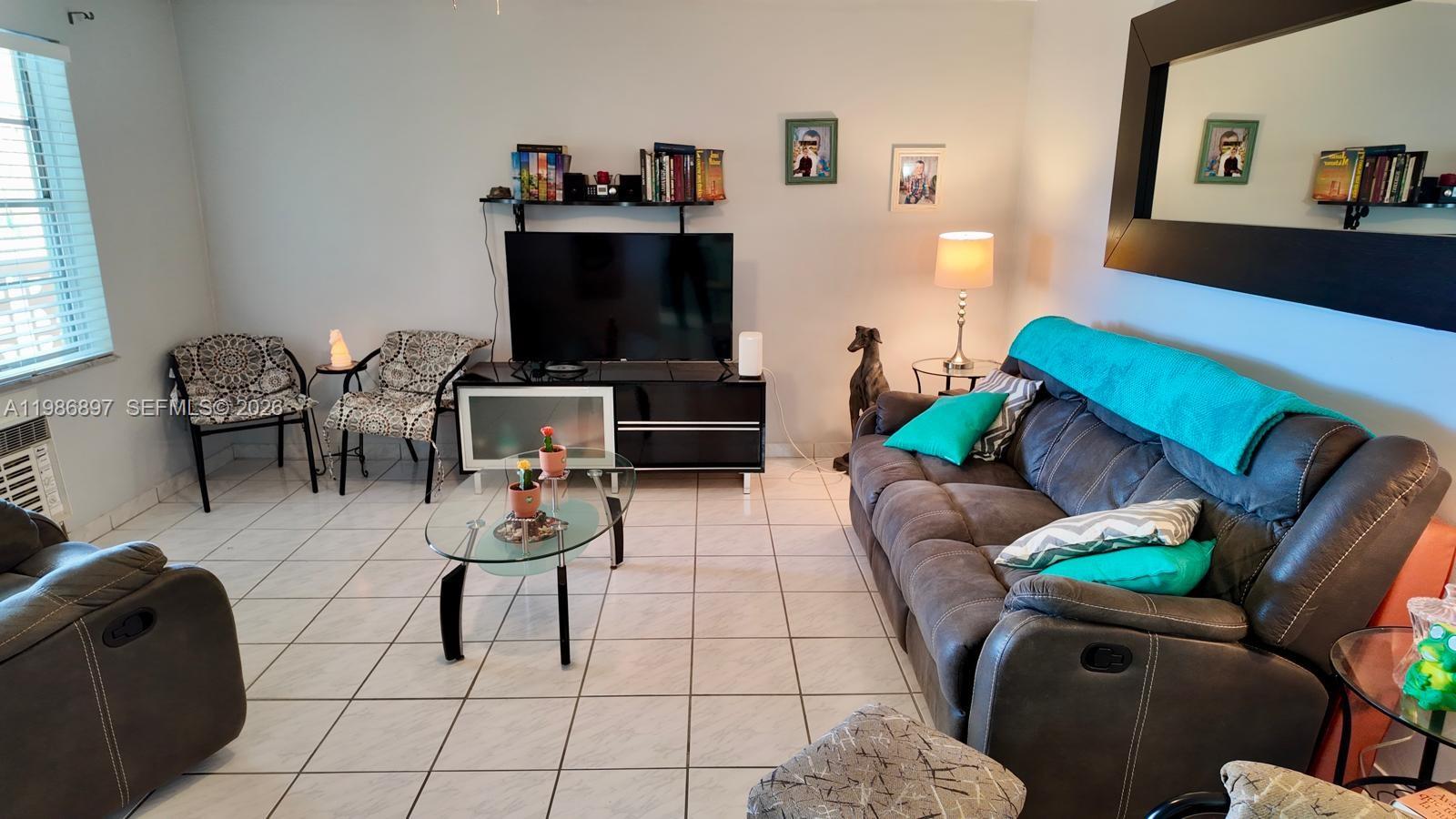 A living room features tile flooring, a dark sofa, a television console, and a coffee table — 16901 NE 13th Ave # 307, Miami FL 33162, MIAMI, FL