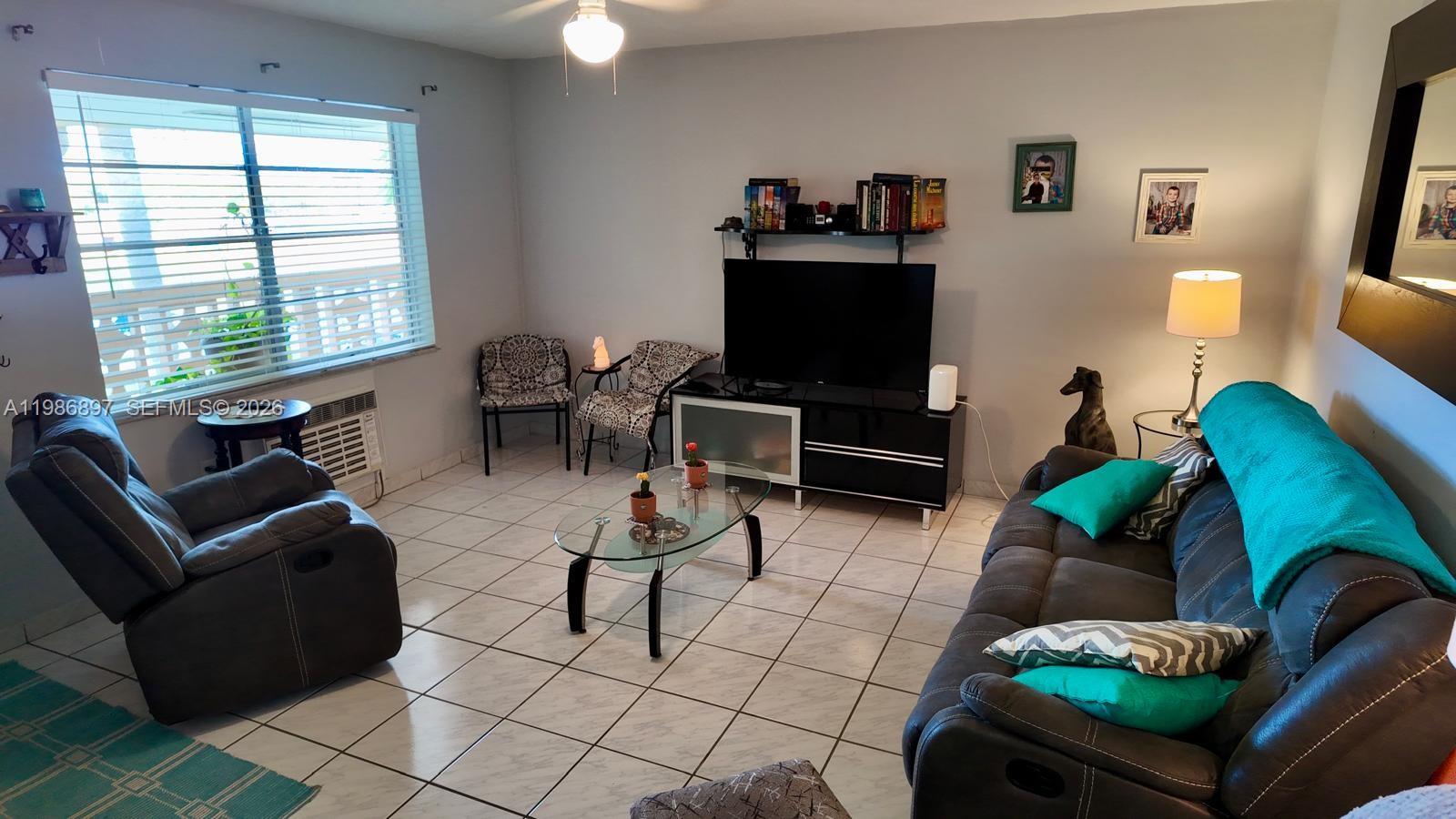A living room features a dark sofa, a recliner, a glass coffee table, and tile flooring — 16901 NE 13th Ave # 307, Miami FL 33162, MIAMI, FL