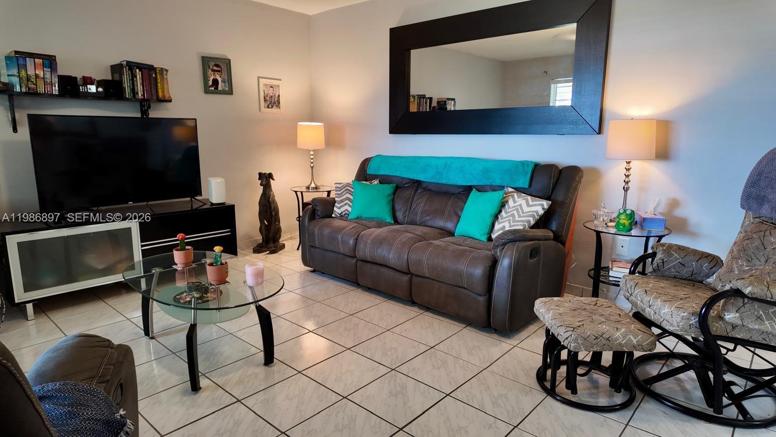 A living room features a brown sofa, a glass coffee table, and a large wall mirror — 16901 NE 13th Ave # 307, Miami FL 33162, MIAMI, FL