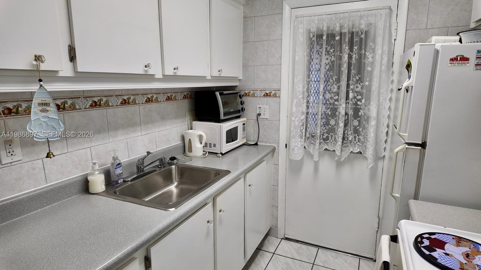 A kitchen features white cabinets, a stainless steel sink, gray countertops, and tiled walls — 16901 NE 13th Ave # 307, Miami FL 33162, MIAMI, FL