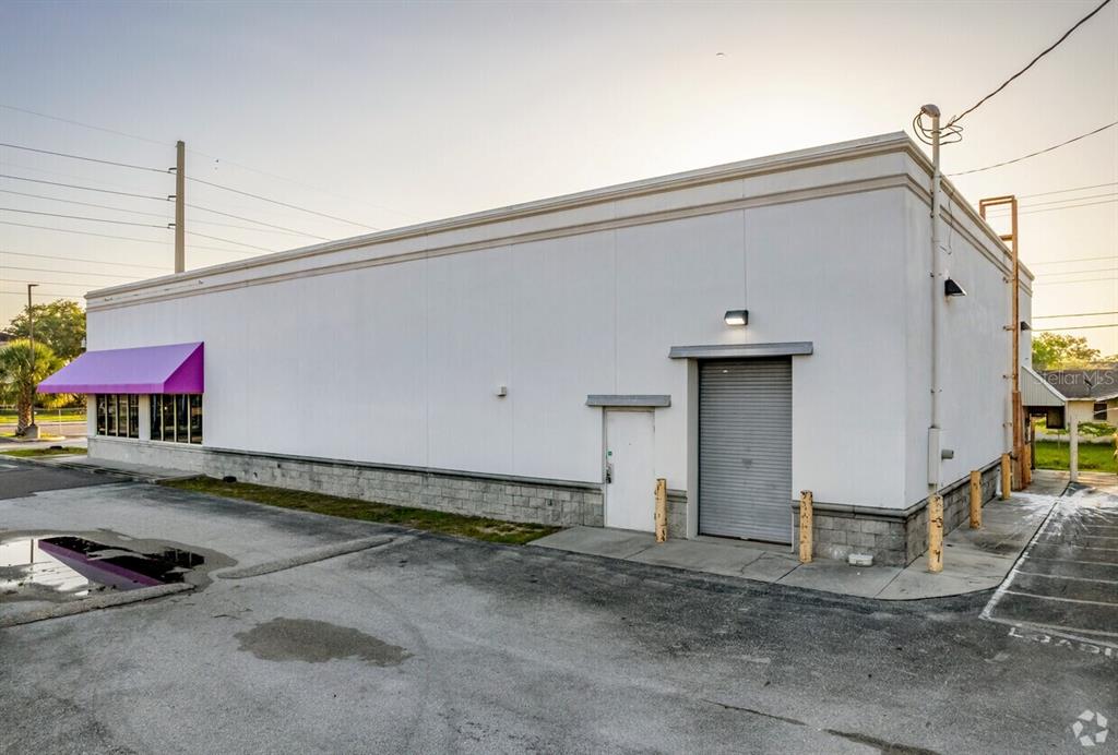 The exterior of a white commercial building features a purple awning and a roll-up door — 1905 CORTEZ ROAD W, BRADENTON, FL