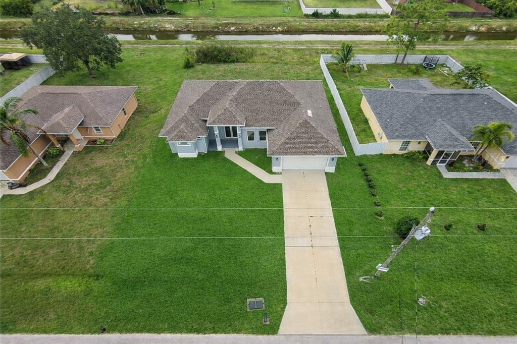 An aerial view shows a single-story house with a driveway and lawn between two neighbors — 1043 ALBERT AVE, LEHIGH ACRES, FL