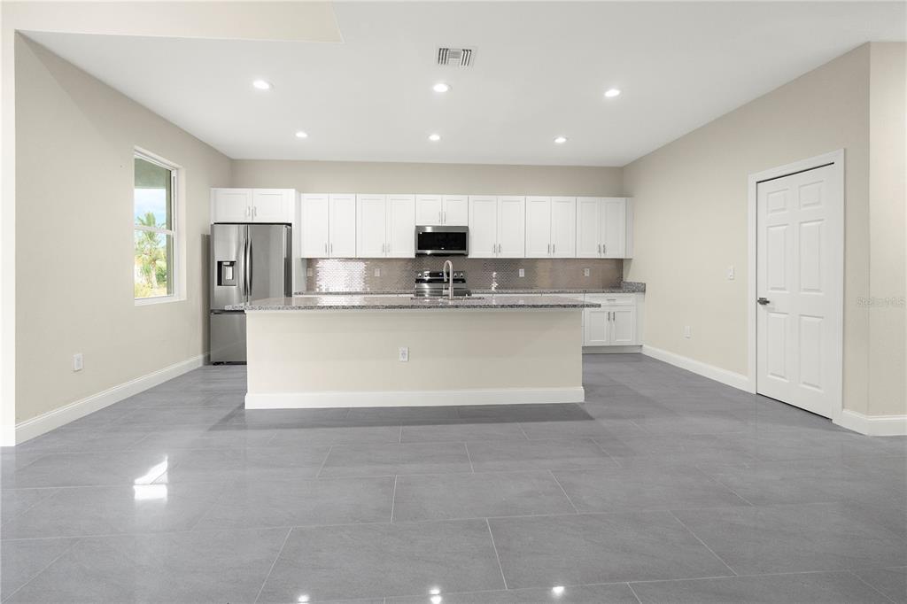 A modern kitchen features white cabinets, granite countertops, stainless steel appliances, and gray tile flooring — 1043 ALBERT AVE, LEHIGH ACRES, FL
