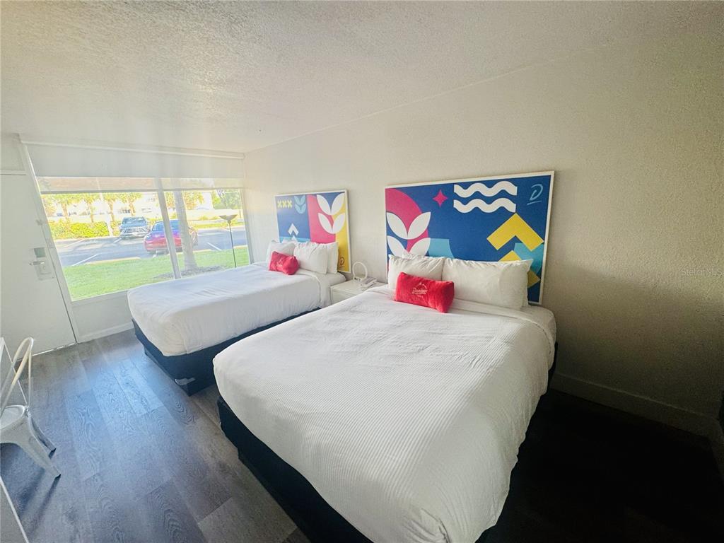 A hotel room features two beds with colorful headboards, wood-look flooring, and a large window — 2930 POLYNESIAN ISLE BOULEVARD UNIT 107, KISSIMMEE, FL