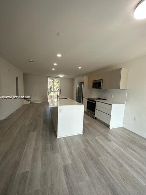 A modern kitchen features a white island, light wood cabinets, and gray wood-look flooring — 2561 NE 193rd St # 1208, Miami FL 33180, MIAMI, FL