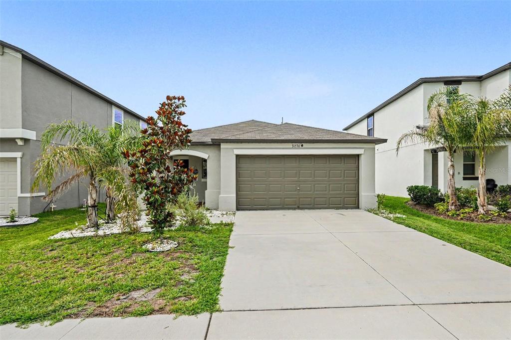 A single-story house with a tan stucco exterior, a two-car garage, and a concrete driveway — 31536 BARREL WAVE WAY, WESLEY CHAPEL, FL