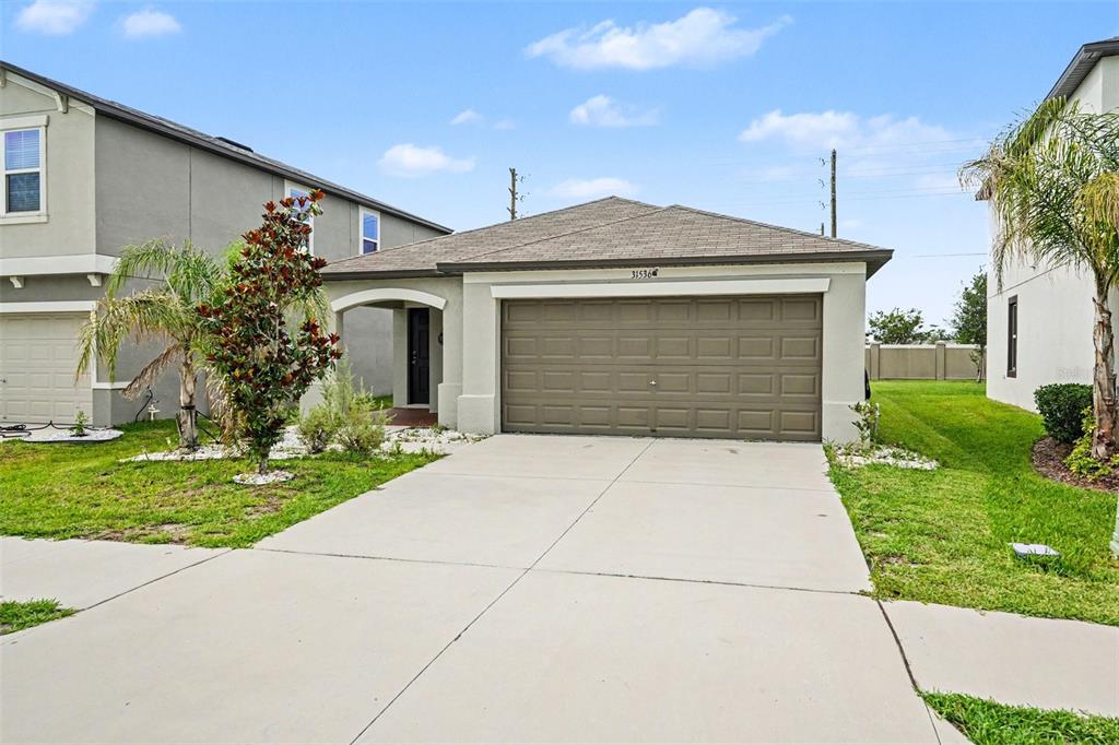 A single-story house with a tan stucco exterior, a two-car garage, and a concrete driveway — 31536 BARREL WAVE WAY, WESLEY CHAPEL, FL