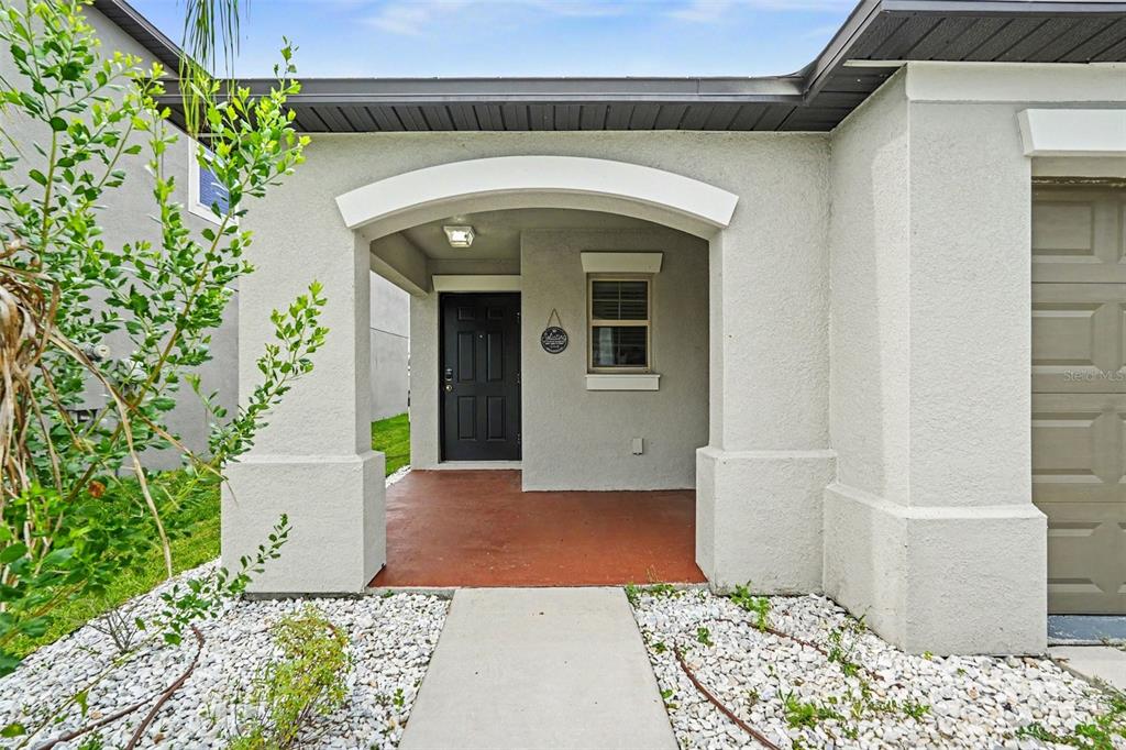 A covered entryway features a dark front door, a window, and a concrete walkway — 31536 BARREL WAVE WAY, WESLEY CHAPEL, FL