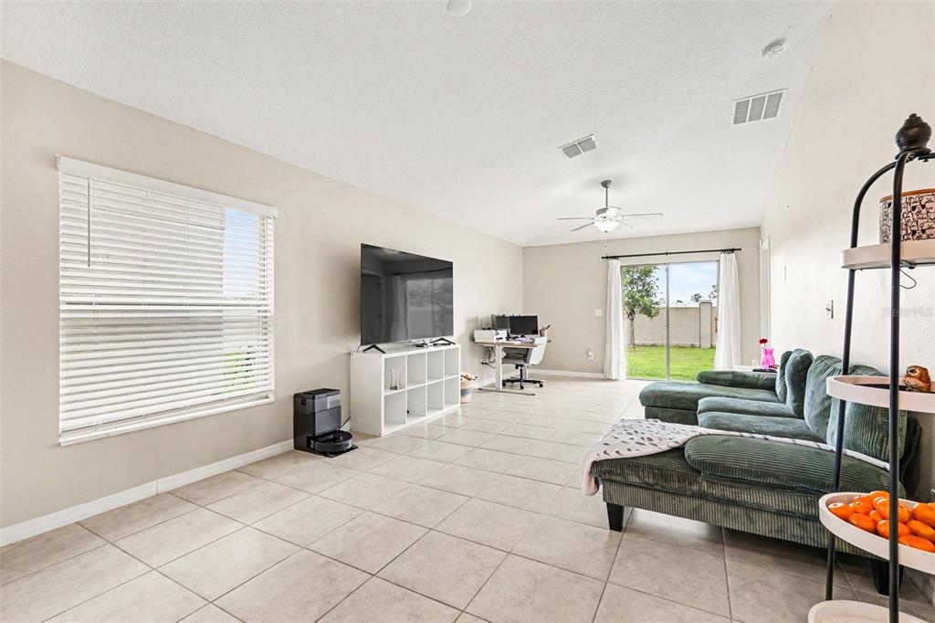 A living room features tile flooring, a large sectional sofa, a television, and sliding glass doors — 31536 BARREL WAVE WAY, WESLEY CHAPEL, FL