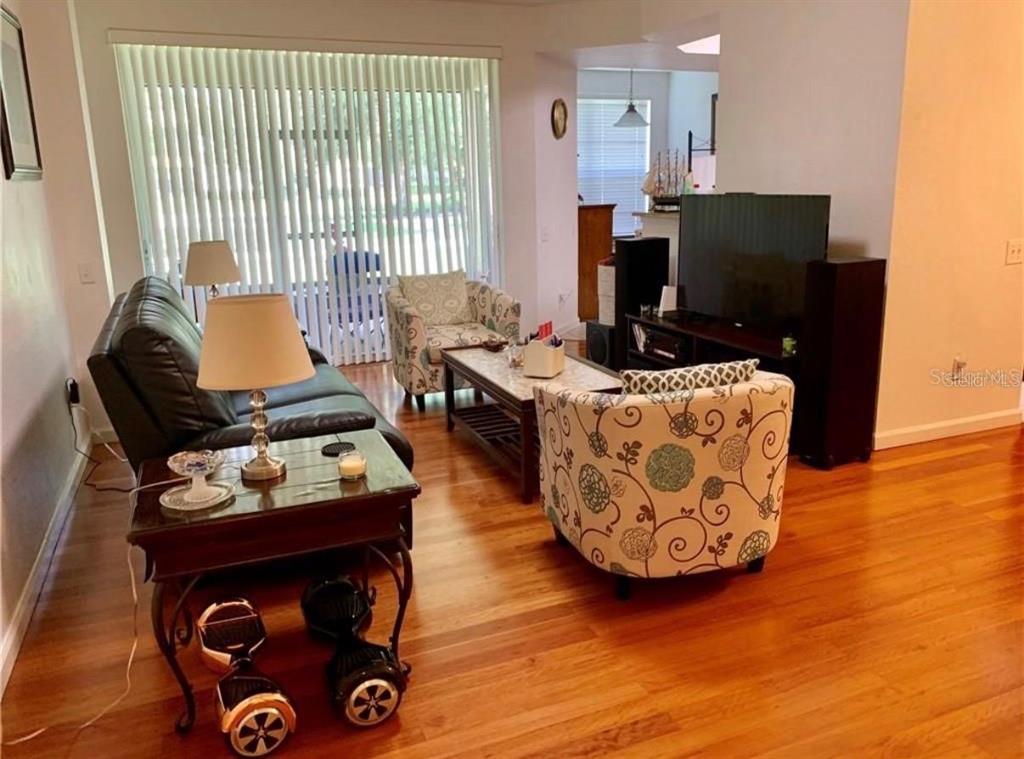 A living room features hardwood floors, a black leather sofa, patterned armchairs, and a television — 2576 SAN TECLA STREET UNIT 107, ORLANDO, FL