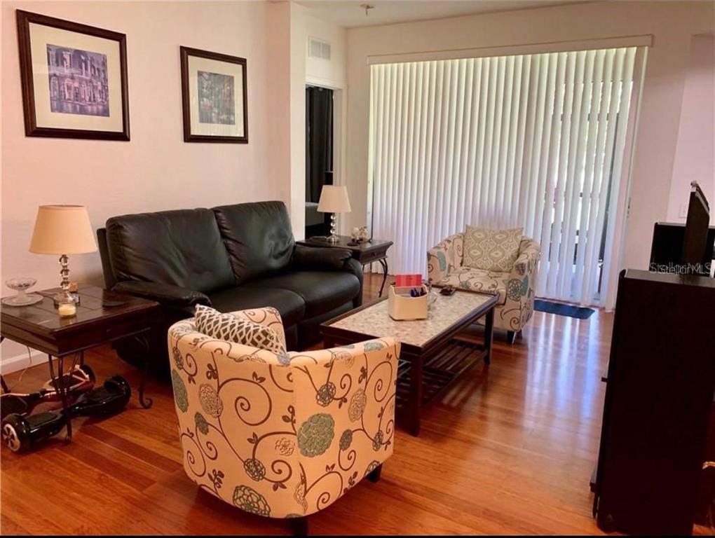 A living room features a black leather sofa, patterned armchairs, and hardwood flooring — 2576 SAN TECLA STREET UNIT 107, ORLANDO, FL