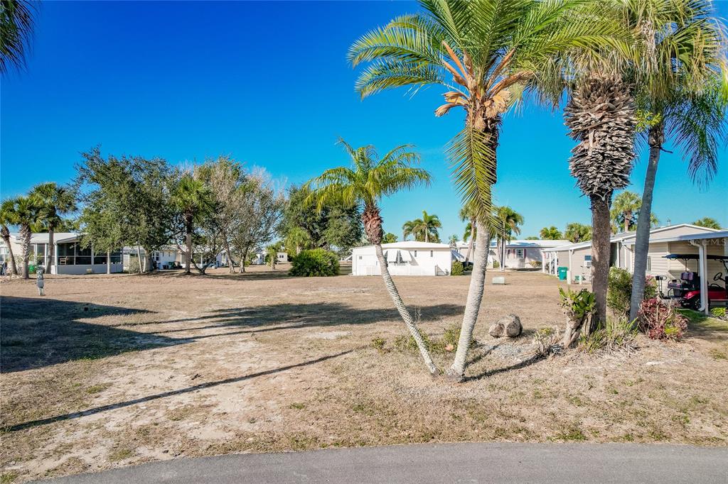 An open, grassy lot with palm trees and surrounding mobile homes under a clear sky — 2100 KINGS HIGHWAY UNIT 1092, PORT CHARLOTTE, FL