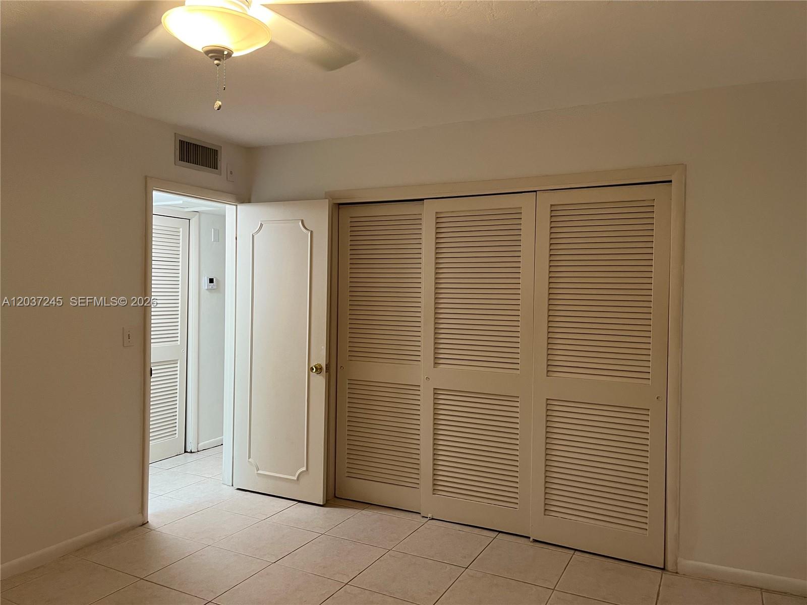 A room with tiled floors, a ceiling fan, and a large louvered closet door — 255 Sunrise Dr # 103, Key Biscayne FL 33149, KEY BISCAYNE, FL