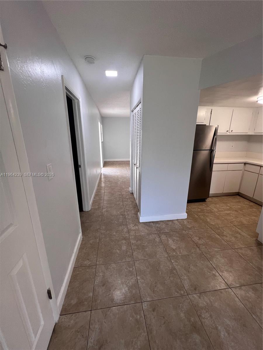 A tiled hallway leads past a kitchen with white cabinets and a stainless steel refrigerator — 5782 SW 61st St # 5782, Miami FL 33143, MIAMI, FL