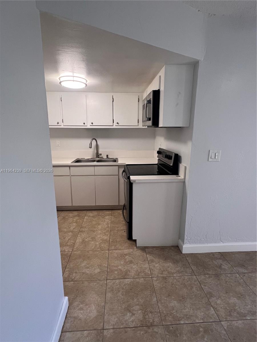 A small kitchen features white cabinets, a black stove, and light-colored tile flooring — 5782 SW 61st St # 5782, Miami FL 33143, MIAMI, FL