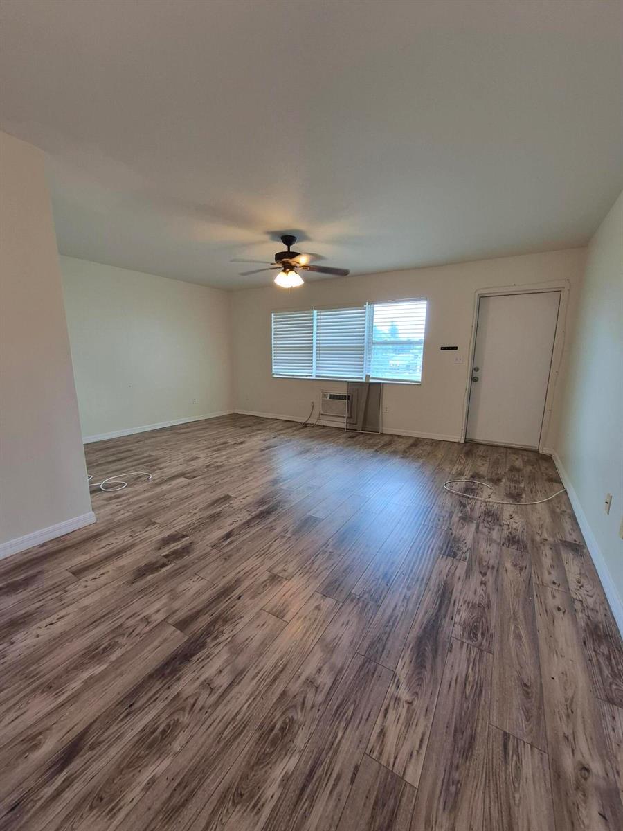 An empty room features wood-look laminate flooring, a ceiling fan, and a window air conditioner — 27 Easthampton B, West Palm Beach FL 33417, WEST PALM BEACH, FL