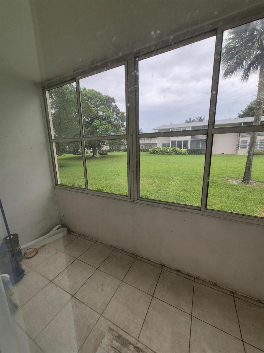 A tiled sunroom features large windows overlooking a grassy lawn and a neighboring building — 27 Easthampton B, West Palm Beach FL 33417, WEST PALM BEACH, FL