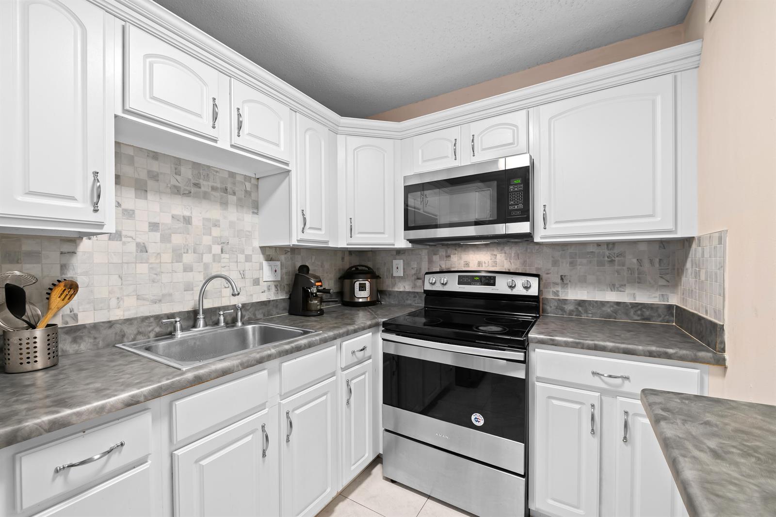 A kitchen features white cabinets, a stainless steel stove, a microwave, and gray countertops — 5180 E Sabal Palm Boulevard # 239, Tamarac FL 33319, TAMARAC, FL