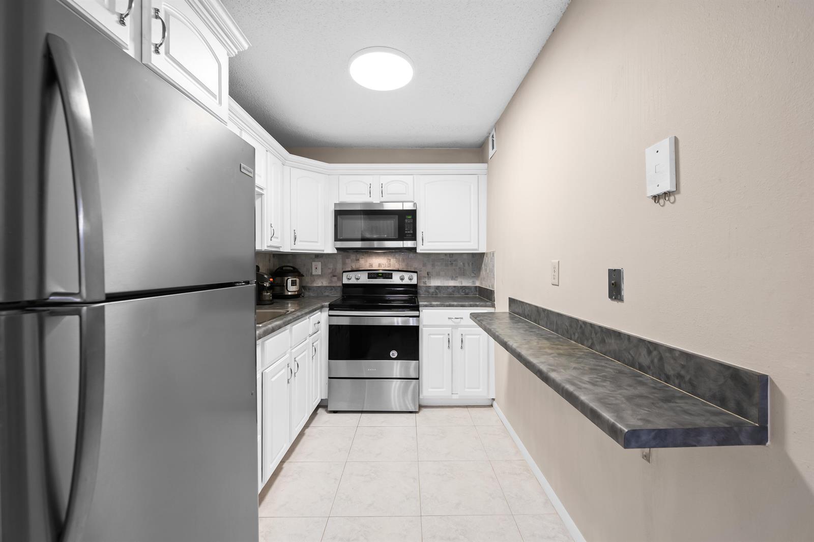 A kitchen features white cabinets, stainless steel appliances, tile flooring, and a wall-mounted breakfast bar — 5180 E Sabal Palm Boulevard # 239, Tamarac FL 33319, TAMARAC, FL