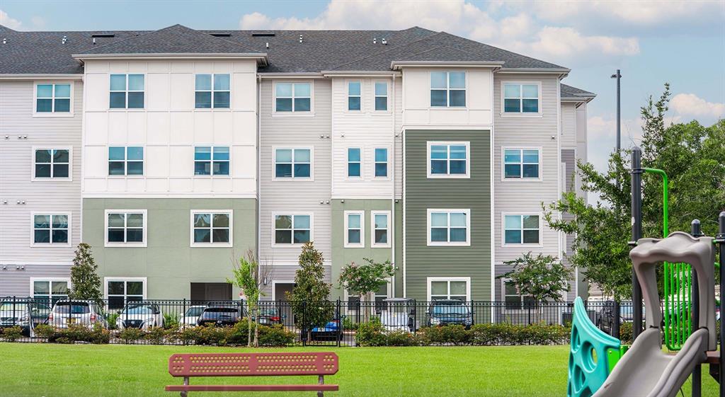 A multi-story apartment building stands behind a grassy lawn with a playground and bench — 110 ZORA PLACE UNIT C1, ORLANDO, FL