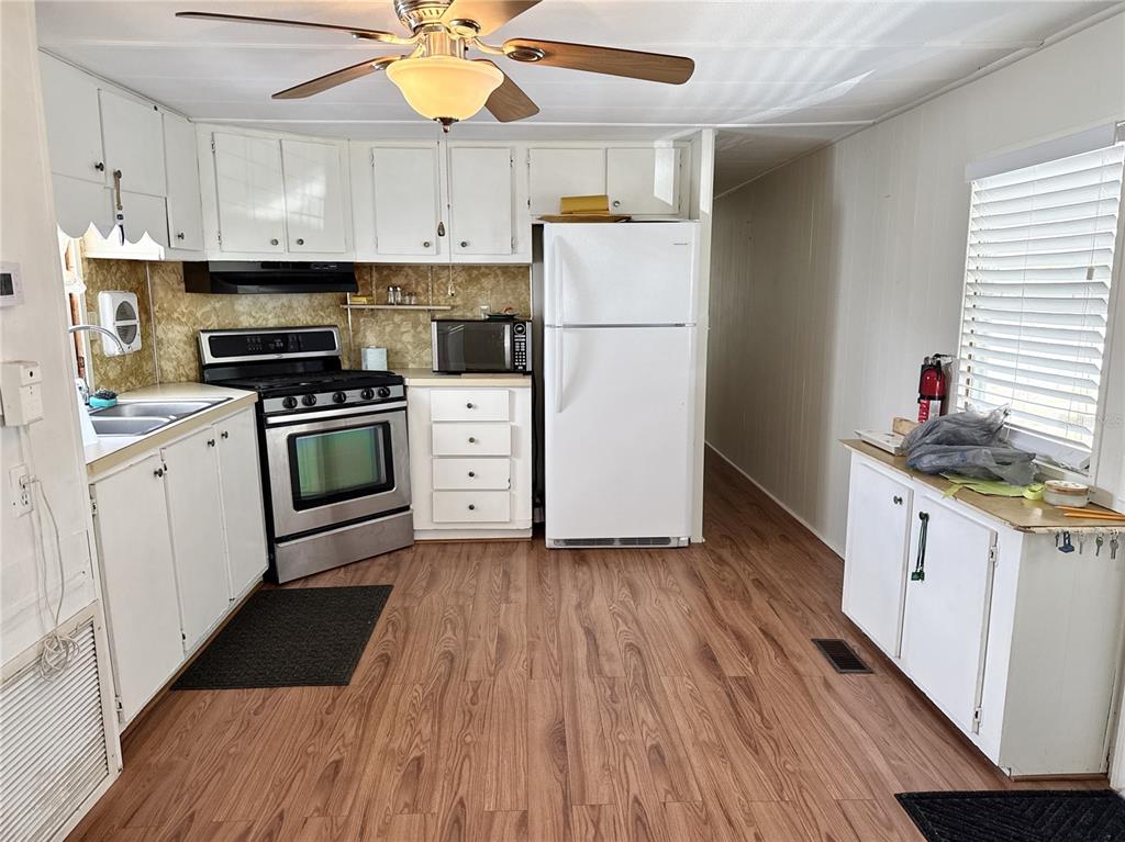 A kitchen features white cabinets, stainless steel appliances, wood-look flooring, and a ceiling fan — 425 MOUNT PINEY AVENUE NE UNIT 681, ST PETERSBURG, FL