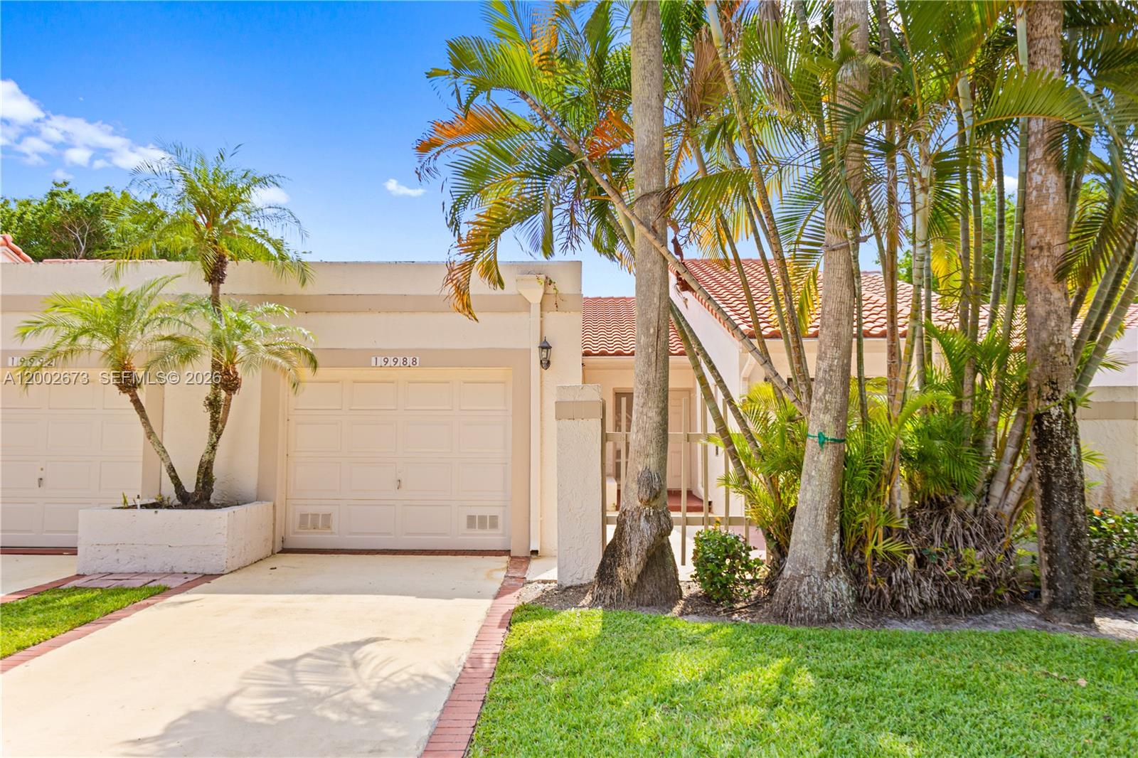 The exterior of a single-story home features a garage, a driveway, and palm trees — 19988 Rima Cir, Boca Raton FL 33434, BOCA RATON, FL