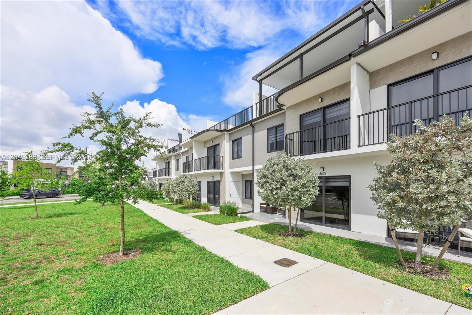 A multi-story townhouse exterior features balconies, sliding glass doors, and a landscaped lawn area — 26122 SW 146th Ave, Homestead FL 33032, HOMESTEAD, FL