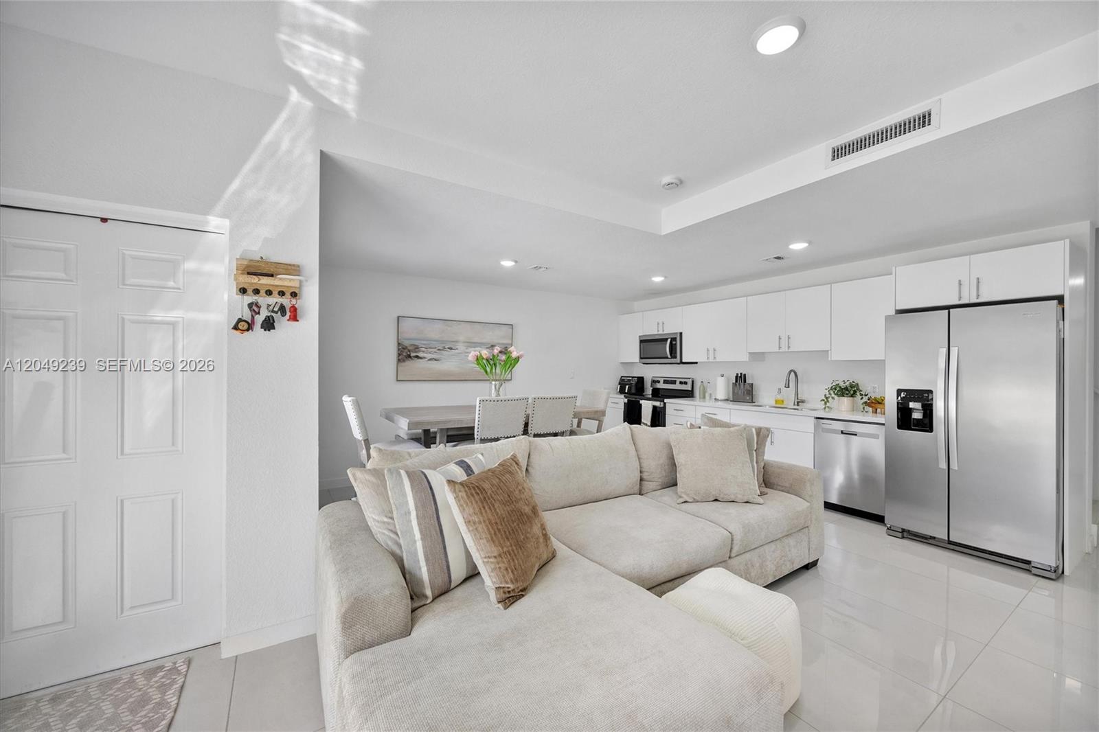 A modern open-concept living room and kitchen feature white cabinets, stainless appliances, and tile flooring — 26122 SW 146th Ave, Homestead FL 33032, HOMESTEAD, FL