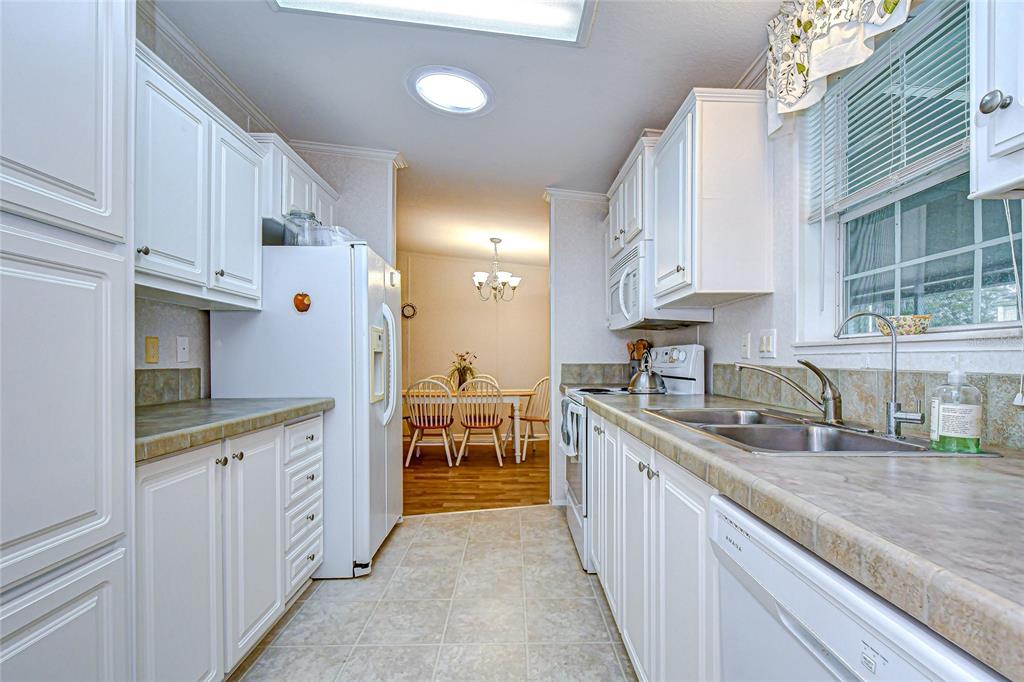 A galley kitchen with white cabinets, laminate countertops, and a view into the dining area — 3337 DAWNS DELL, ZEPHYRHILLS, FL