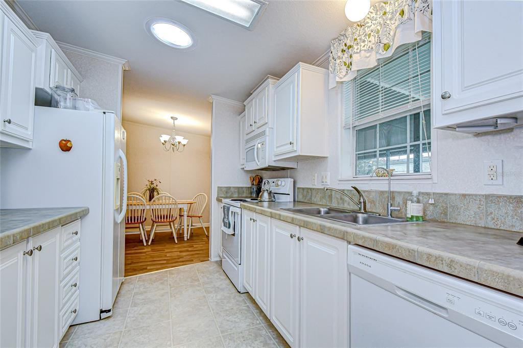 A kitchen with white cabinets, laminate countertops, and a dining area visible in the background — 3337 DAWNS DELL, ZEPHYRHILLS, FL