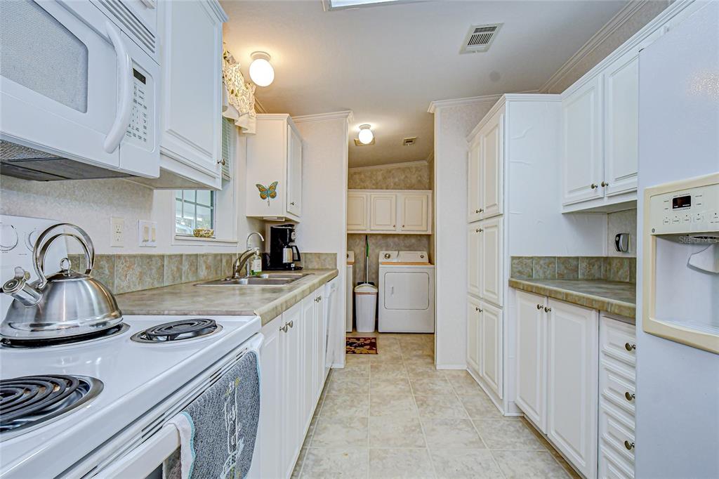 A kitchen with white cabinetry, laminate countertops, and a laundry area in the background — 3337 DAWNS DELL, ZEPHYRHILLS, FL