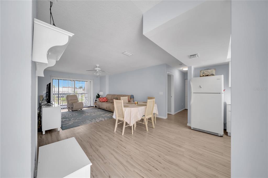 An open-concept living and dining area features light wood-look flooring and a white refrigerator — 1318 WESLEY DRIVE UNIT 124B, PUNTA GORDA, FL
