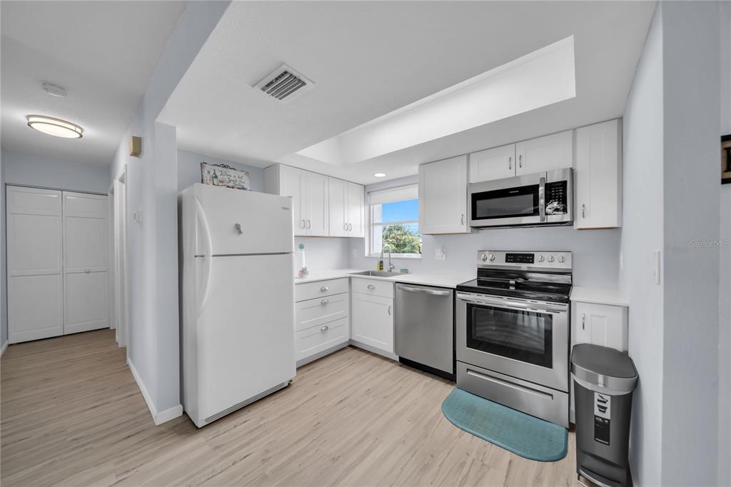 A kitchen features white cabinets, stainless steel appliances, and light wood-look flooring — 1318 WESLEY DRIVE UNIT 124B, PUNTA GORDA, FL
