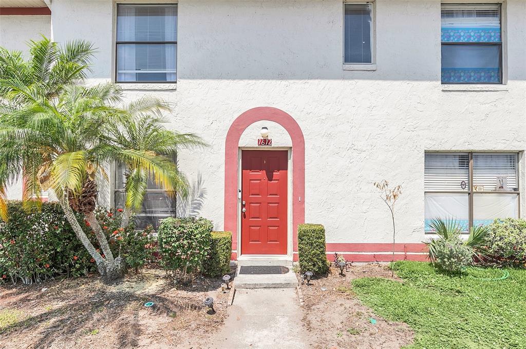 A two-story white stucco building features a red front door and a palm tree — 1612 SANDY POINT SQUARE UNIT 56, ORLANDO, FL