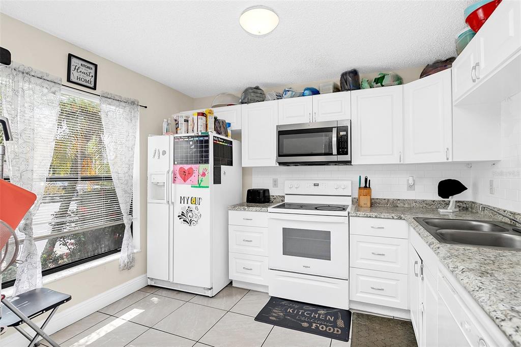 A kitchen features white cabinetry, granite countertops, a white refrigerator, and a white electric range — 1612 SANDY POINT SQUARE UNIT 56, ORLANDO, FL