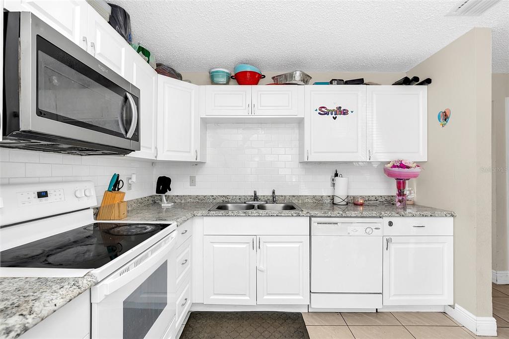A kitchen features white cabinets, granite countertops, a subway tile backsplash, and stainless steel appliances — 1612 SANDY POINT SQUARE UNIT 56, ORLANDO, FL