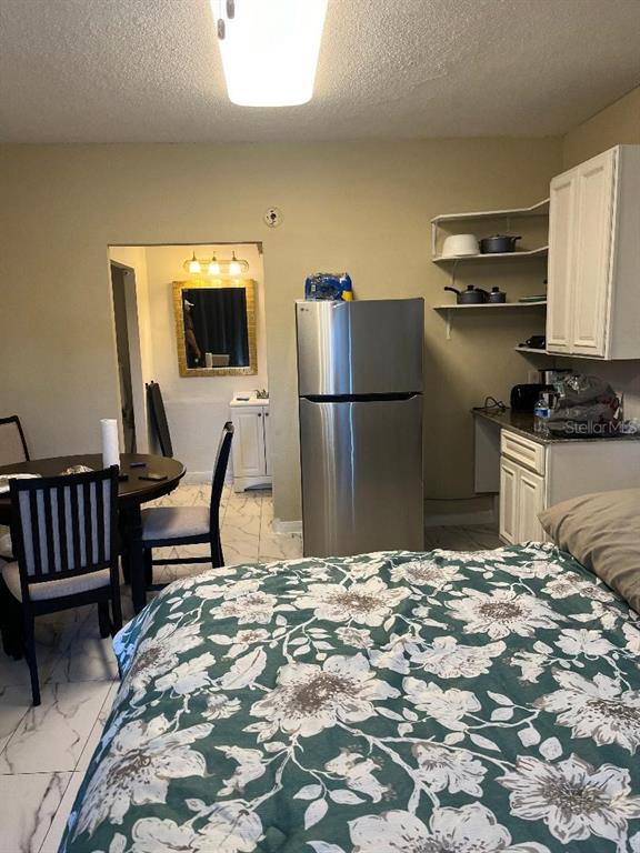 A bedroom with a dining table, stainless steel refrigerator, and open shelving in the kitchen — 8421 S ORANGE BLOSSOM TRAIL UNIT 248, ORLANDO, FL