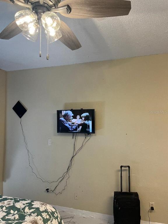 A bedroom features a ceiling fan, a wall-mounted television with visible cords, and a rolling suitcase — 8421 S ORANGE BLOSSOM TRAIL UNIT 248, ORLANDO, FL