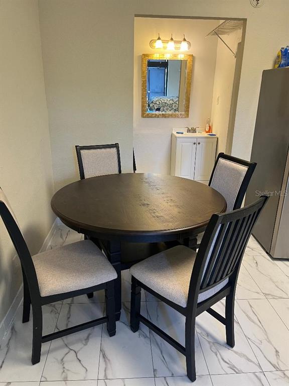 A round wooden dining table with four chairs sits on a white tiled floor — 8421 S ORANGE BLOSSOM TRAIL UNIT 248, ORLANDO, FL