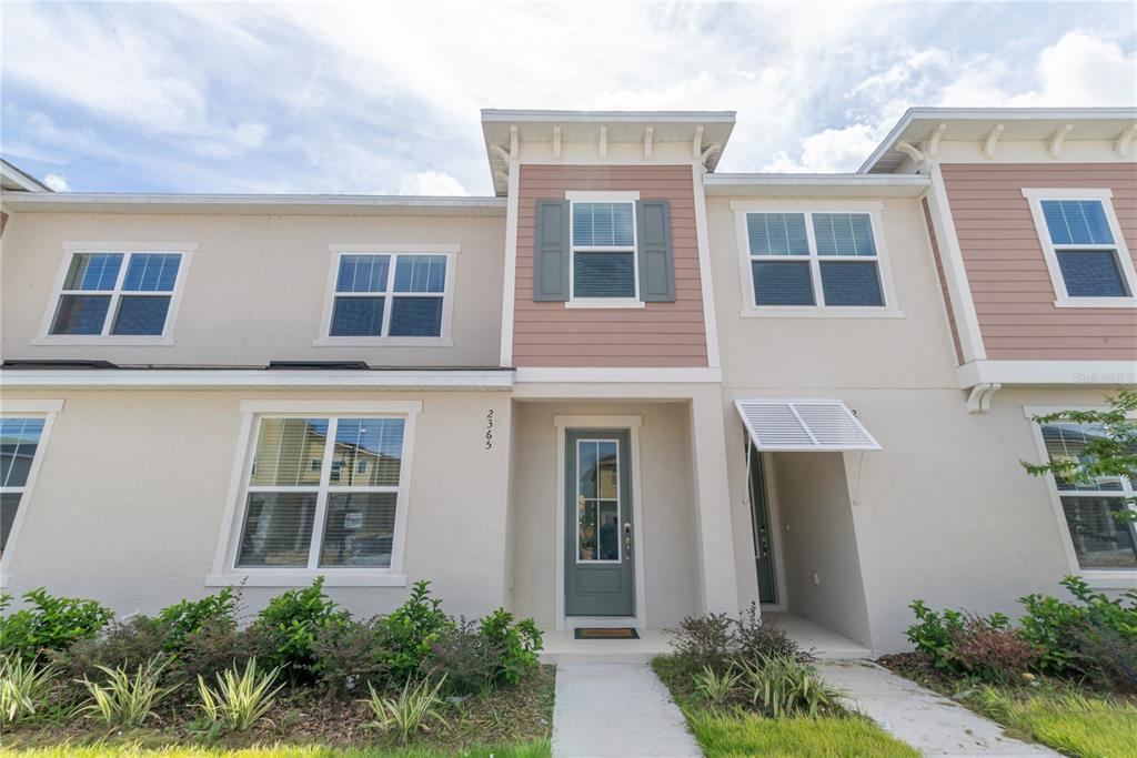 A two-story townhouse exterior features beige stucco, a green front door, and a small walkway — 2365 DISTANT SUN TRAIL, KISSIMMEE, FL