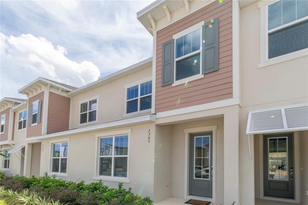 A two-story townhouse exterior features beige stucco, tan siding, and gray shutters under a cloudy sky — 2365 DISTANT SUN TRAIL, KISSIMMEE, FL