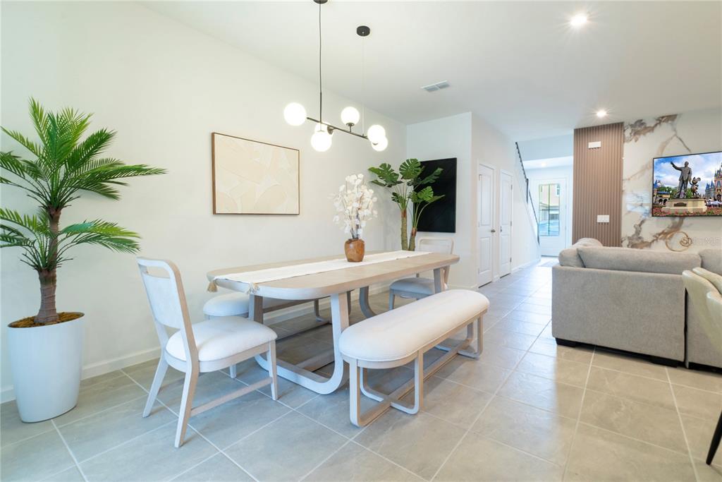 A dining area features a light wood table, white chairs, a bench, and a modern chandelier — 2365 DISTANT SUN TRAIL, KISSIMMEE, FL