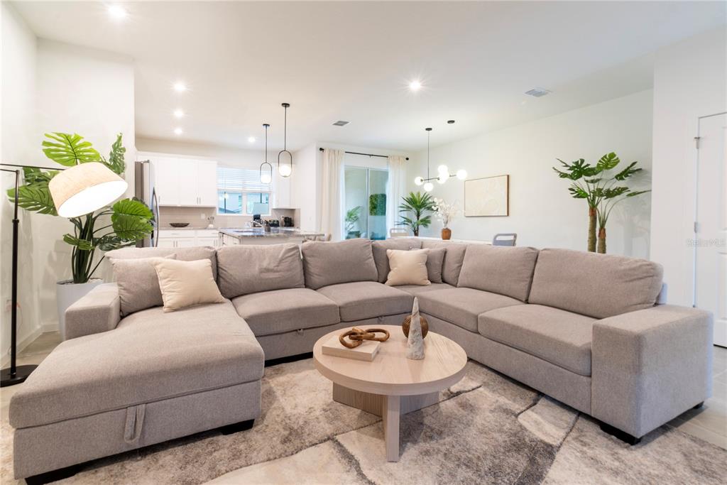 A modern living room features a large gray sectional sofa, a round coffee table, and plants — 2365 DISTANT SUN TRAIL, KISSIMMEE, FL