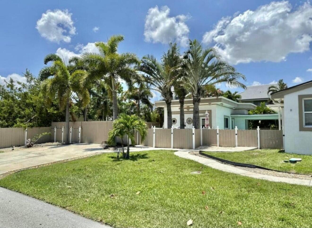 A grassy front yard features a concrete driveway, palm trees, and a tan privacy fence — 698 Forsyth Street # 2, Boca Raton FL 33487, BOCA RATON, FL
