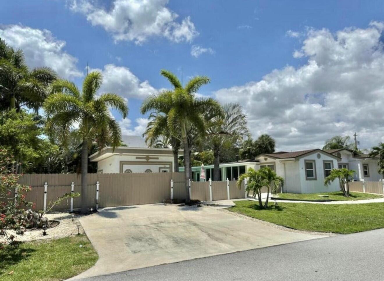 A concrete driveway leads to a house with a tan fence and two palm trees — 698 Forsyth Street # 2, Boca Raton FL 33487, BOCA RATON, FL