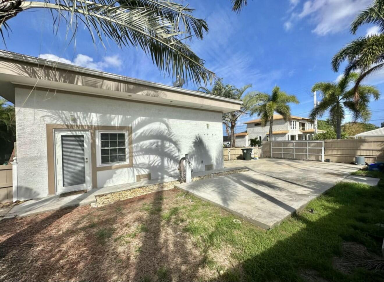 A view of a house exterior with a concrete patio, palm trees, and a fence — 698 Forsyth Street # 2, Boca Raton FL 33487, BOCA RATON, FL